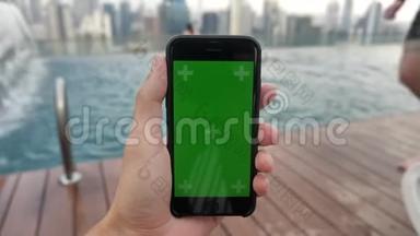 智能手机的特写镜头，绿色屏幕彩色键放在游泳池附近，在触摸屏上观看视频并跟踪